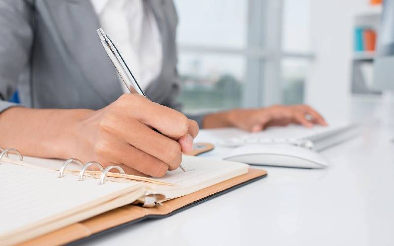 A person writing on paper with a pen.