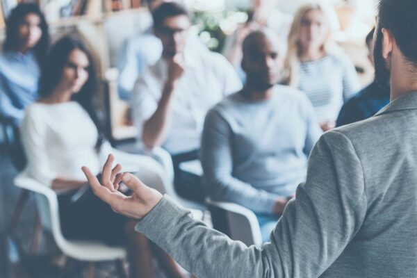 A group of people sitting in front of a person holding their hands up.